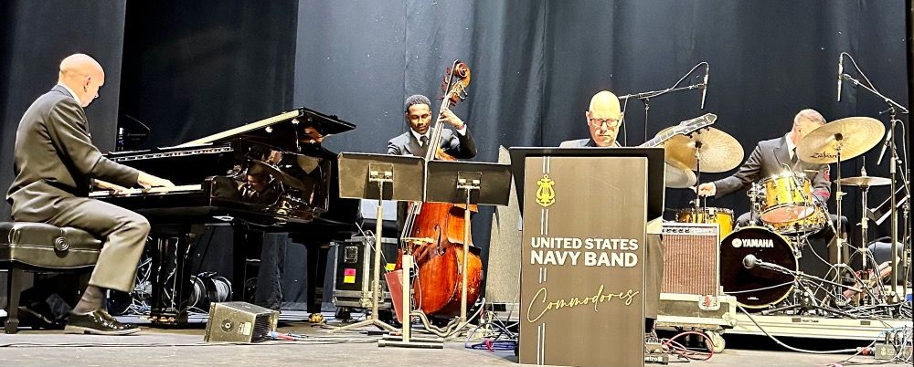 A photo of the pianist, bassist, guitarist, and drummer of the U.S. Navy Band Commodores performing onstage at the Saenger Theatre in Pensacola